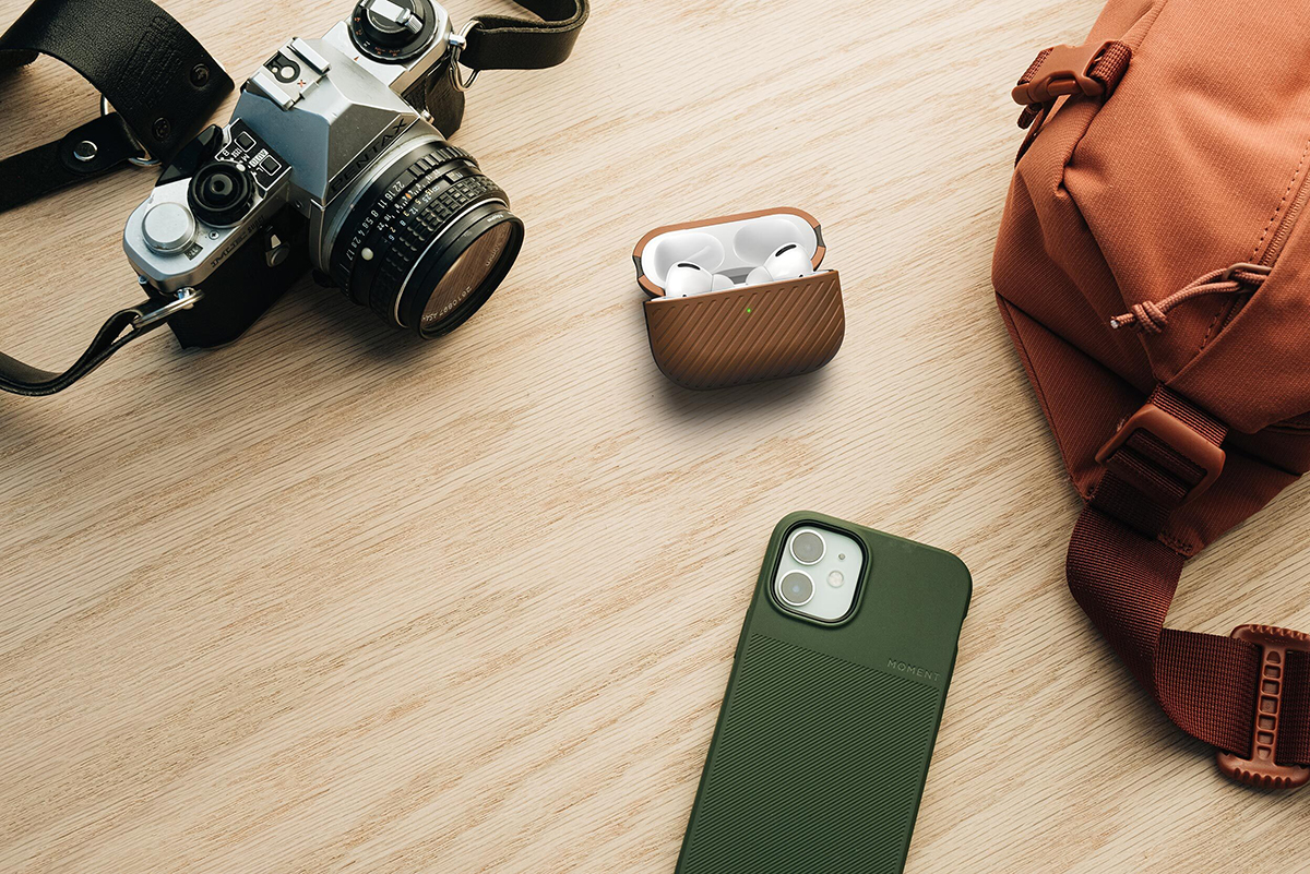 several everyday carry items, including a camera, an iPhone in a protective case, a pair of Apple AirPods